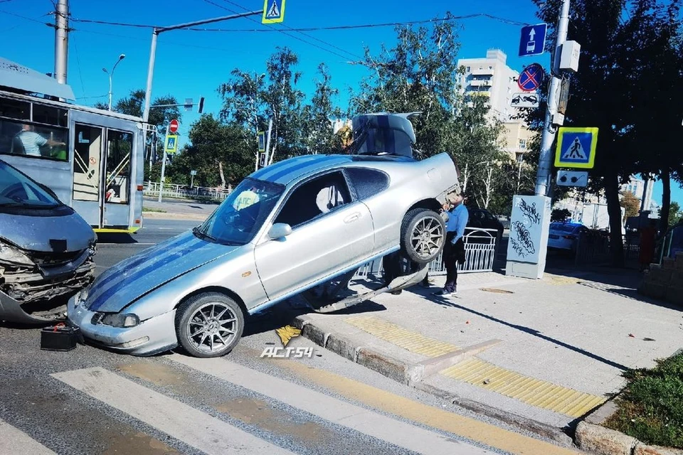 Попавшая в ДТП легковушка повисла задней частью на заборе в Новосибирске. Фото: АСТ-54