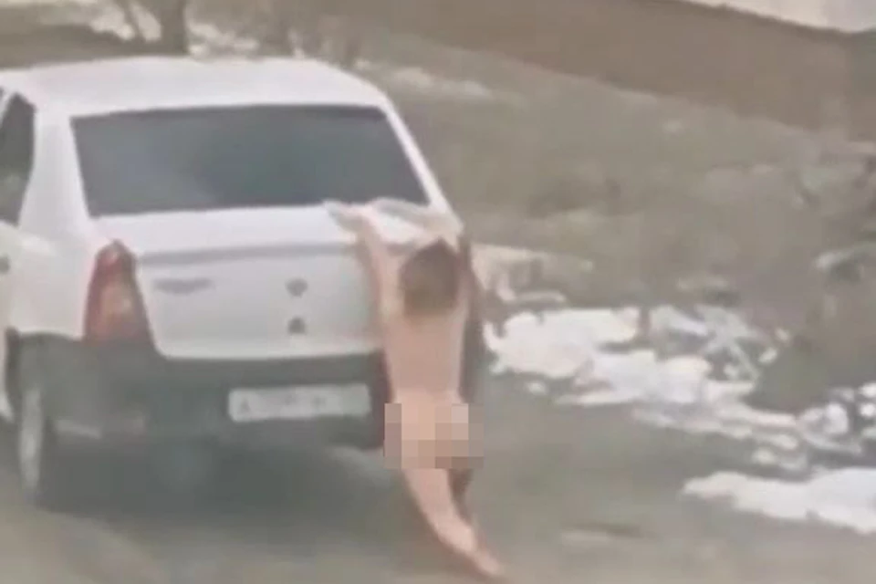 Голая женщина проехала коленями по льду на багажнике машины. Кадр видео.
