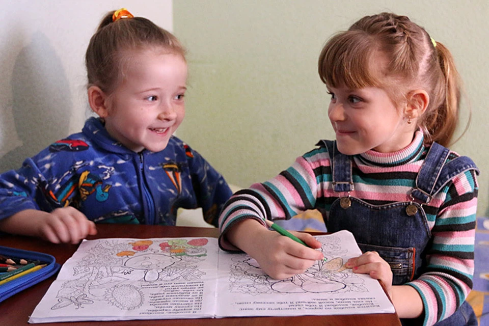В уголке комнаты две девчонки, пыхтя, рисуют в книжке-раскраске