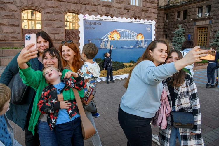 Днем ранее жители Киева с энтузиазмом фотографировались на фоне плаката со взорванным Крымским мостом.